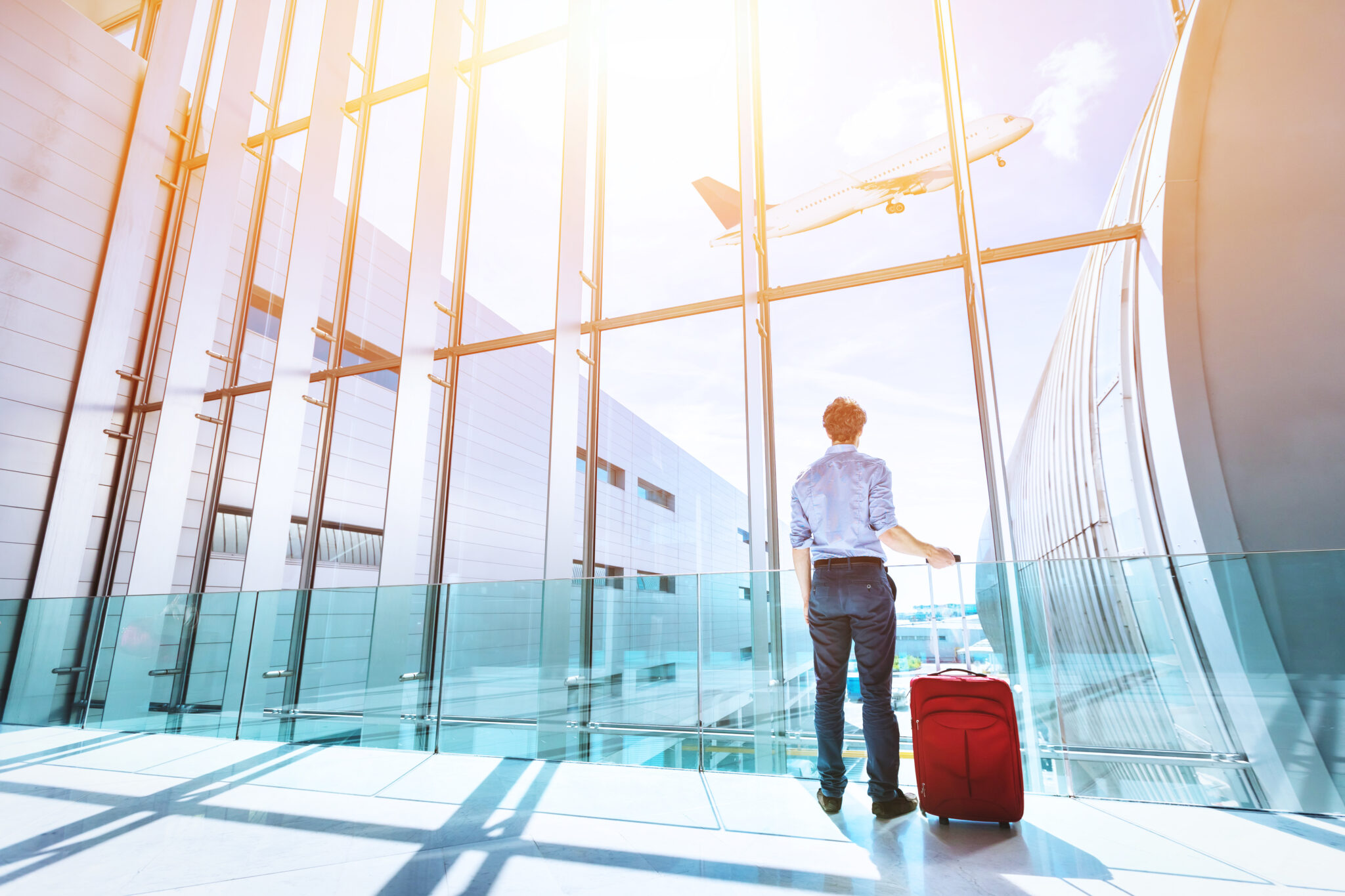 Businessman at airport terminal boarding gate looking at airplane flying through the window